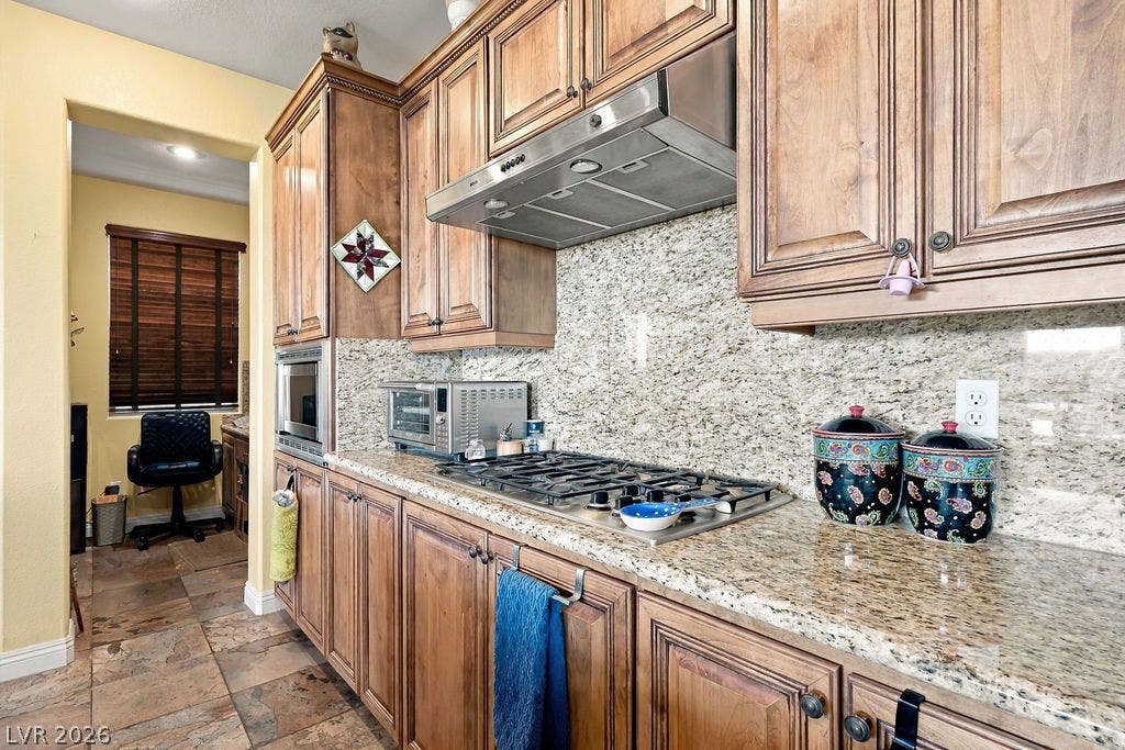 Rich wood cabinetry complements polished stone countertops and textured tile flooring in this cooking space.
