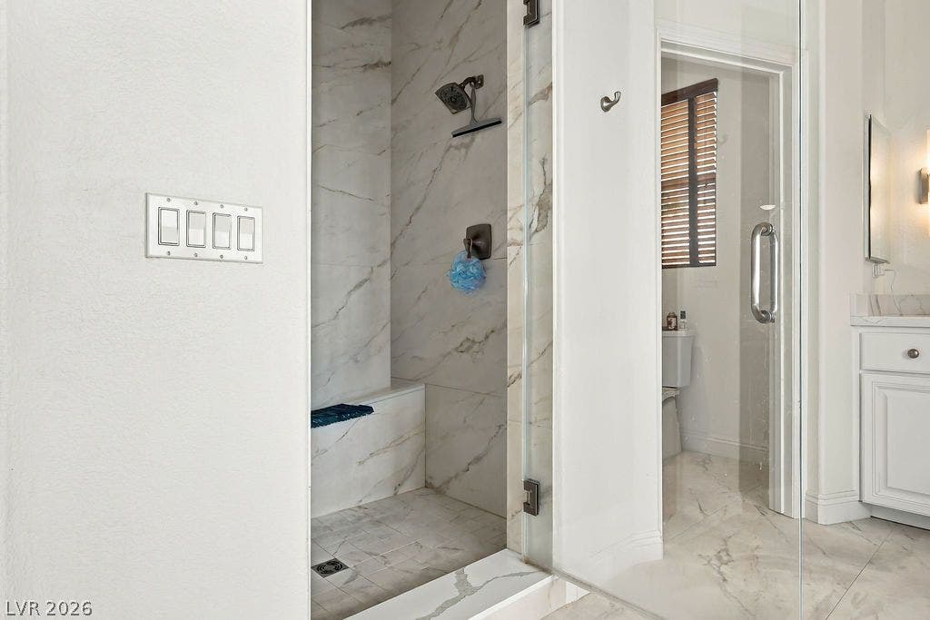 Fine marble tile runs from the floor into a glass-enclosed shower with a bench.
