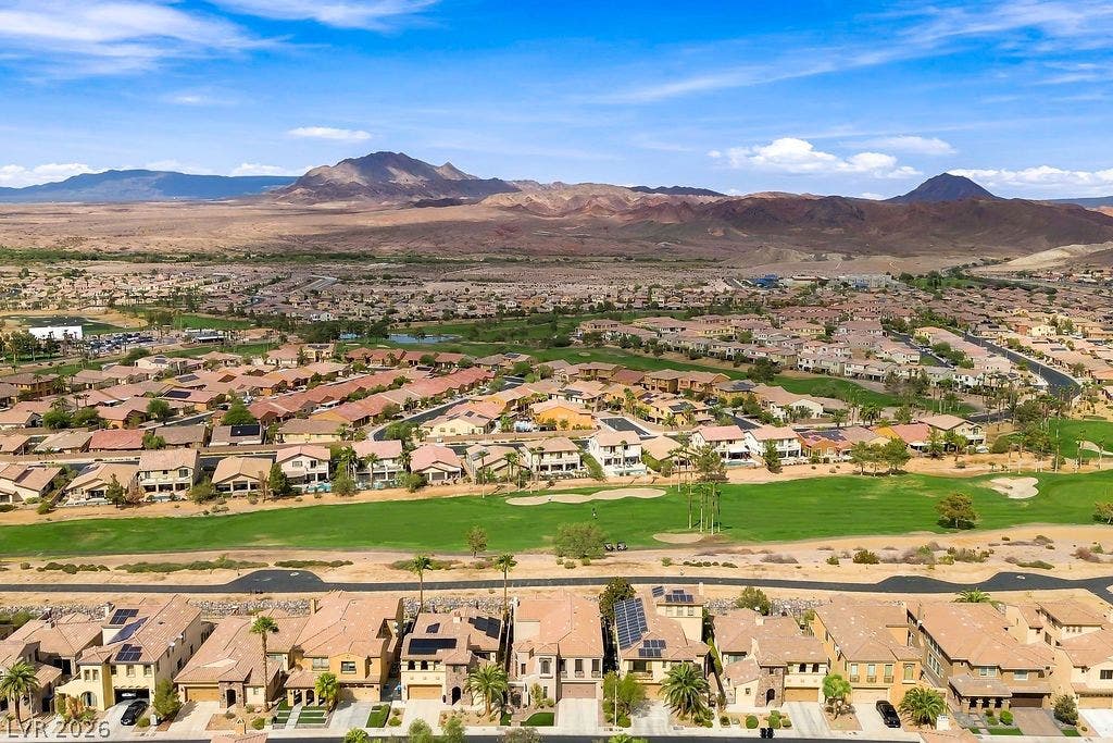 Dramatic mountain ridges frame a vibrant green golf course running through the residential community.