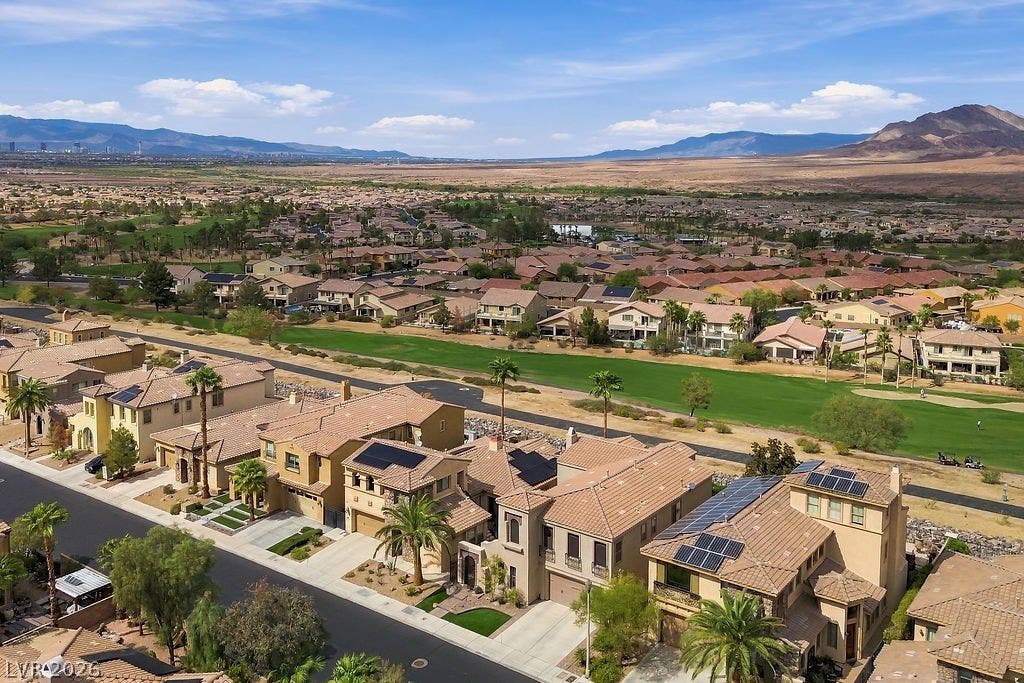 Distant mountains frame a sprawling golf course neighborhood with modern multi-level residences.