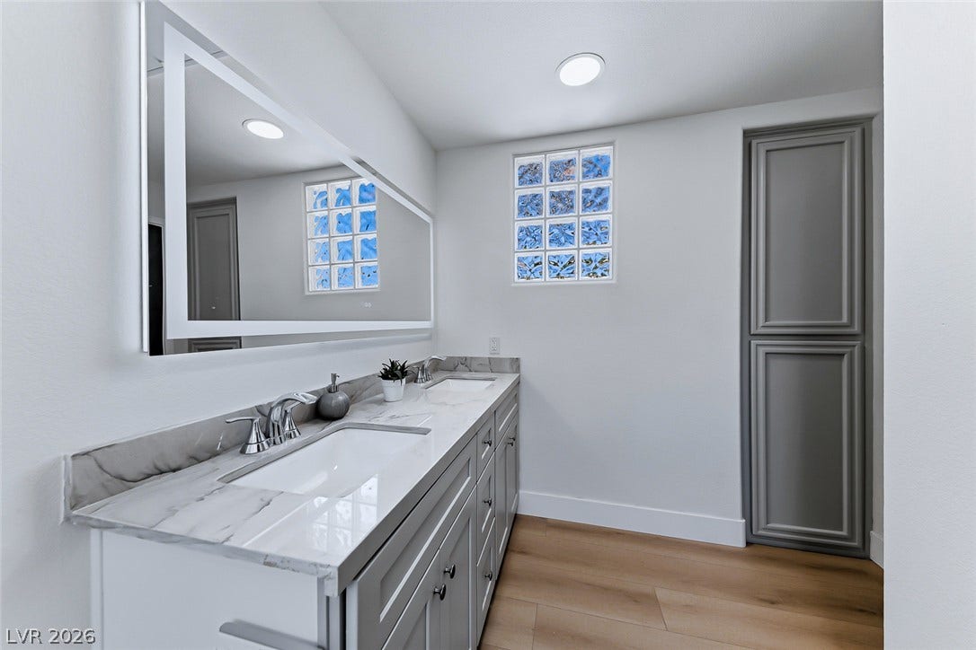 2601 Arimo Drive, Henderson, NV 89052 A long marble-topped double vanity anchors this modern bathroom with warm wood-look flooring.