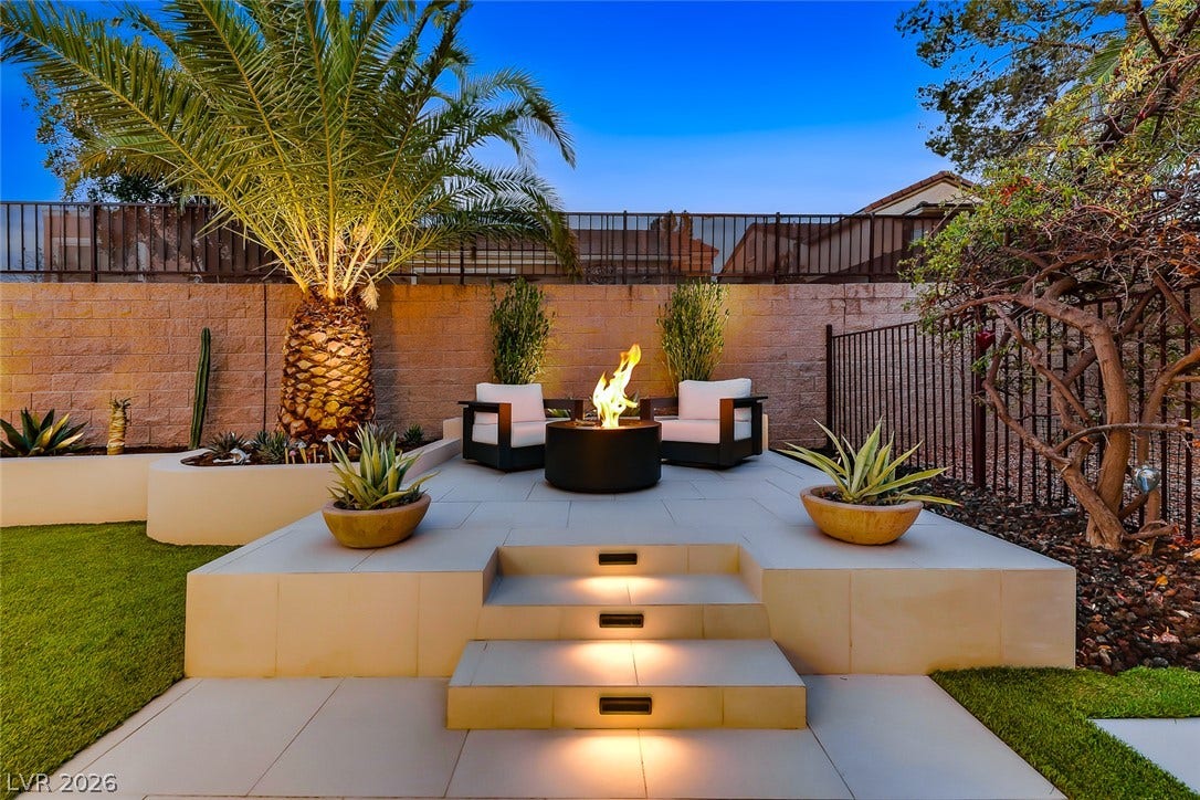 2601 Arimo Drive, Henderson, NV 89052 An inviting stone patio features a raised fire pit lounge beneath a tropical palm tree.