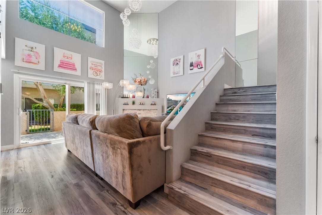 6250 W Flamingo Road, #37, Las Vegas, NV 89103 A grand staircase with sleek wooden steps and a white railing elegantly ascends, complementing the spacious, well-lit living area.