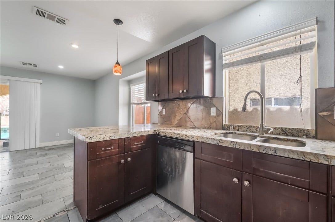 Kitchen featuring dark brown cabinets, stainless steel dishwasher, backsplash, decorative light fixtures, and a peninsula