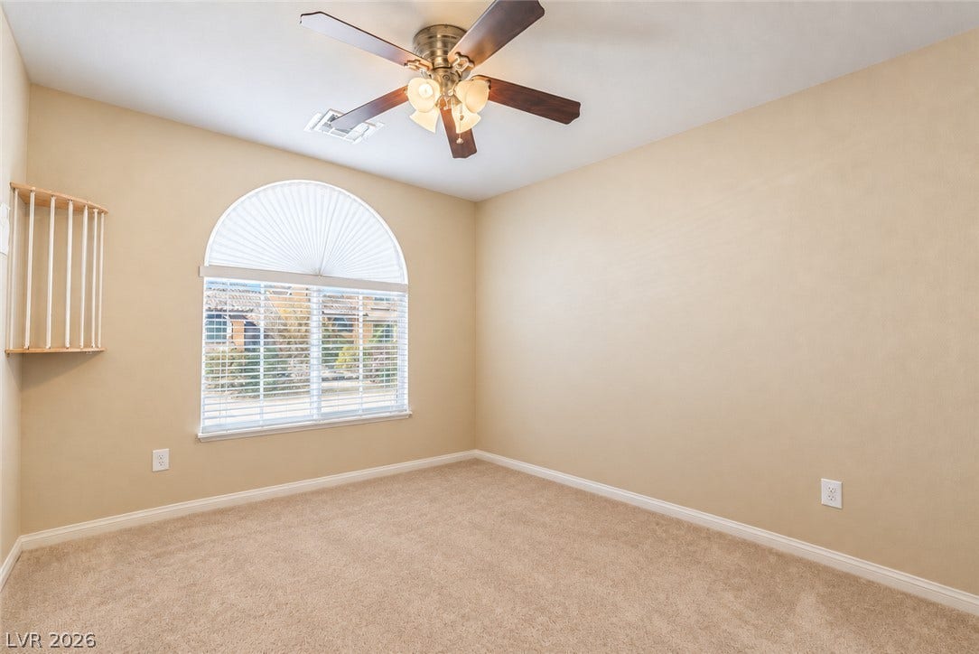 6771 Bravura Court, Las Vegas, NV 89139 A spacious arched window draws natural light across the comfortable carpeted flooring of this room.