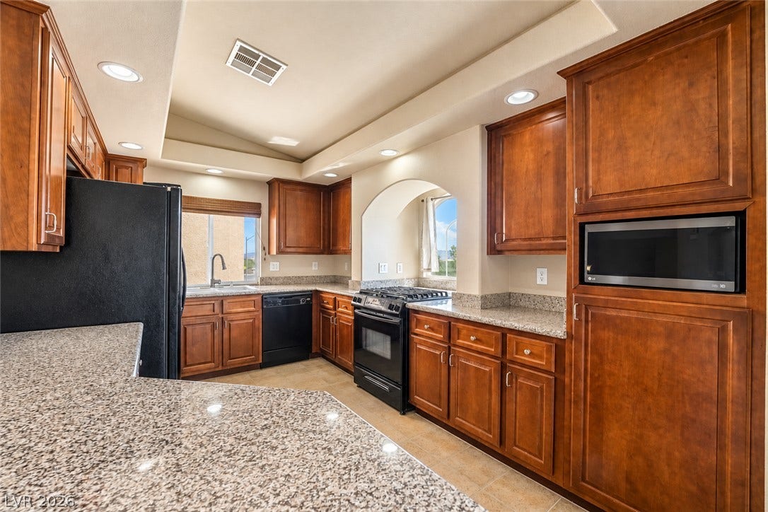 6771 Bravura Court, Las Vegas, NV 89139 Rich wood cabinetry and polished stone countertops elevate this kitchen with recessed lighting.