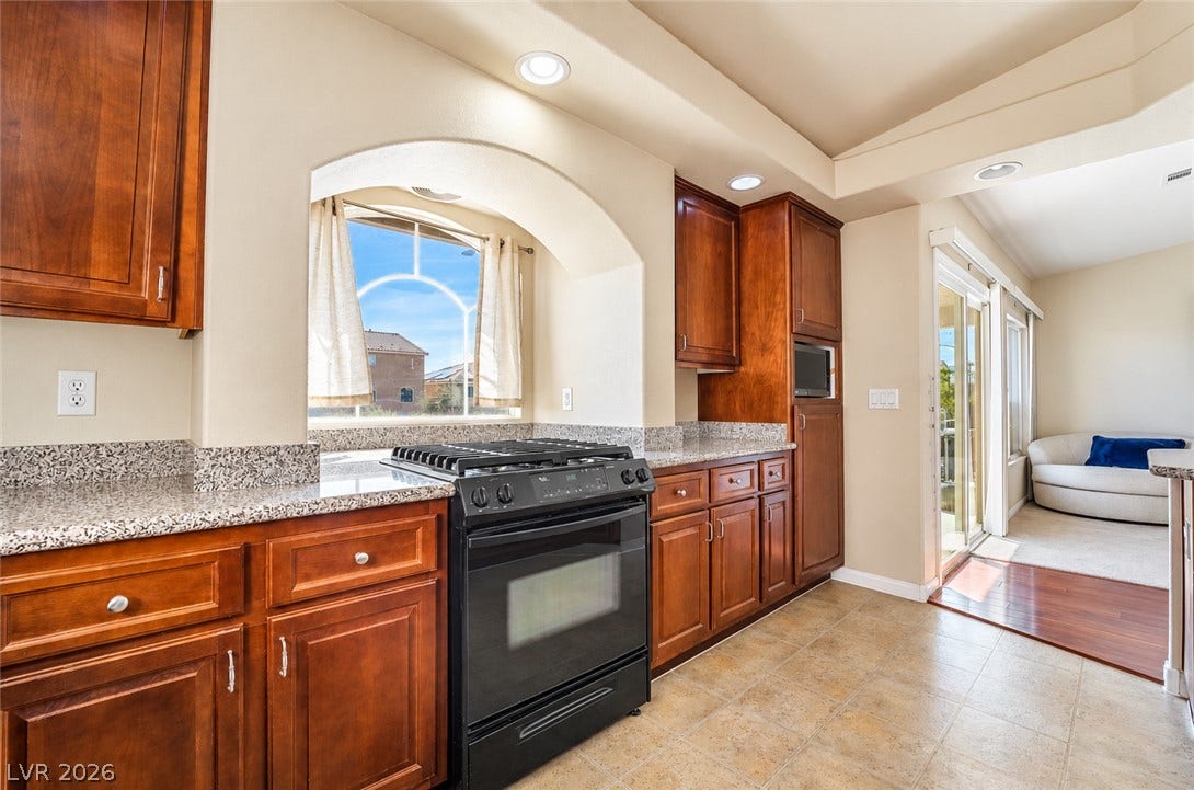6771 Bravura Court, Las Vegas, NV 89139 Rich wood cabinetry and granite countertops frame a central gas range under recessed lighting.