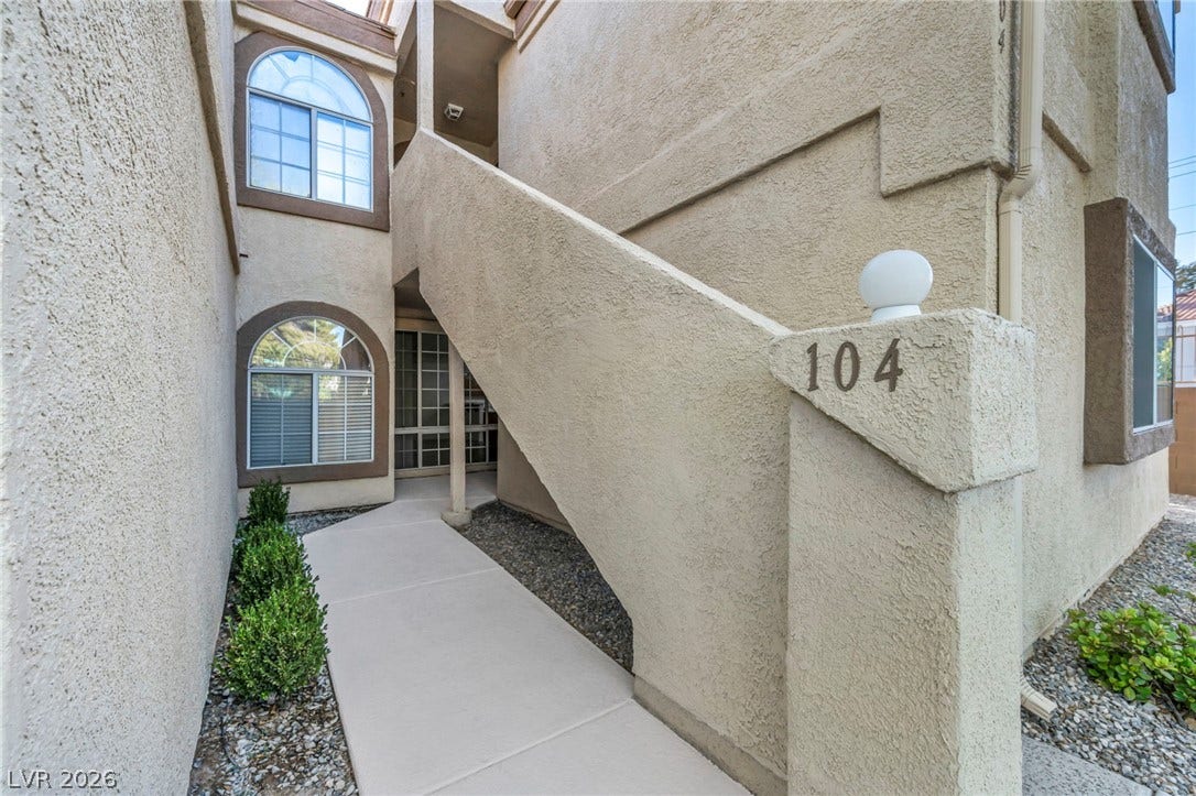 3613 Shawn Reynolds Court, #104, Las Vegas, NV 89129 An inviting concrete walkway leads past manicured exterior walls toward arched windows and outdoor stairs.