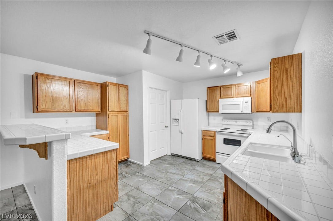 3613 Shawn Reynolds Court, #104, Las Vegas, NV 89129 Tiled countertops and abundant wood cabinetry define this functional, light-filled kitchen space.