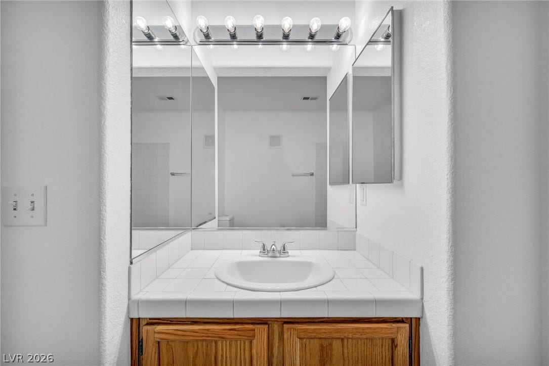 3613 Shawn Reynolds Court, #104, Las Vegas, NV 89129 Tiled countertops and a wood vanity offer classic character in this functional bathroom space.