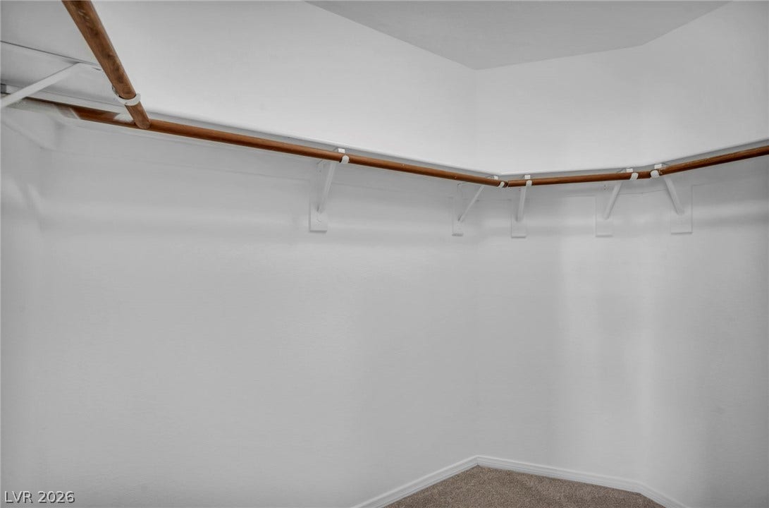3613 Shawn Reynolds Court, #104, Las Vegas, NV 89129 Primary Bedroom - A spacious walk-in closet features soft carpeting and built-in wooden hanging rods.