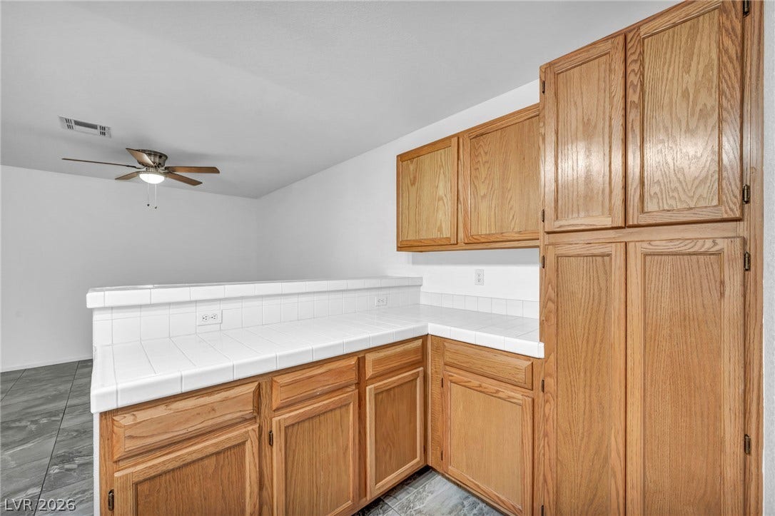 3613 Shawn Reynolds Court, #104, Las Vegas, NV 89129 Natural wood cabinetry offers ample storage alongside clean tiled countertops and tile flooring.
