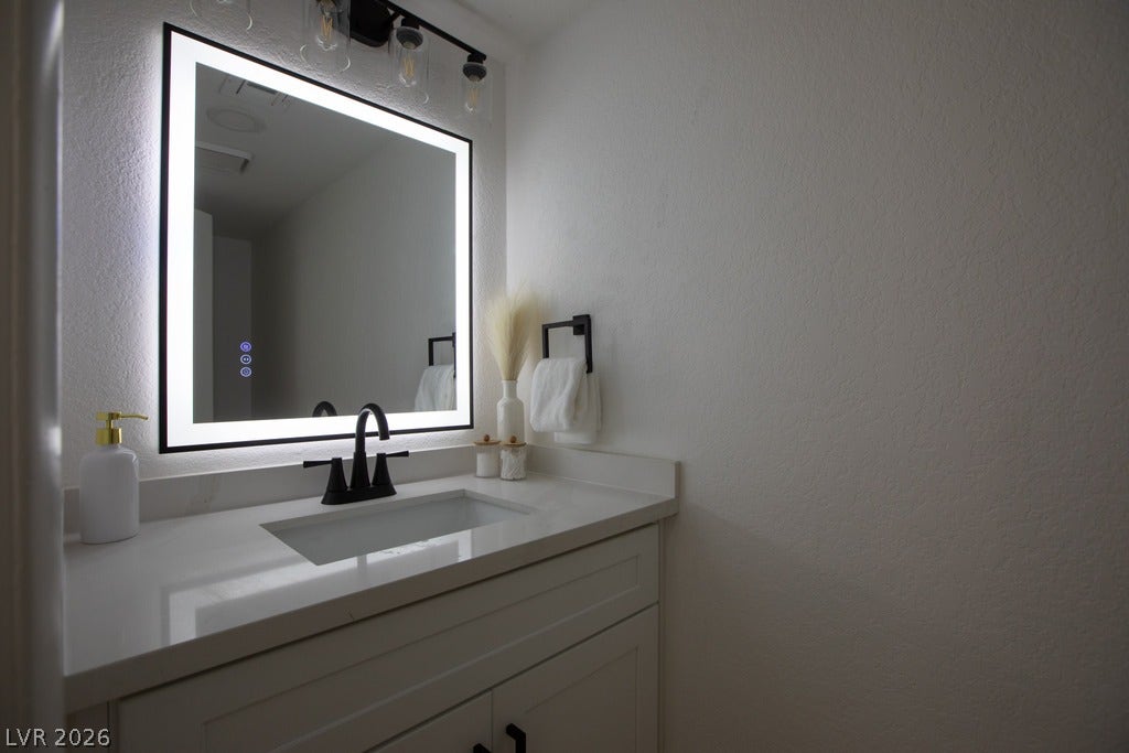 2371 Pickwick Drive, Henderson, NV 89014 A modern vanity features a sleek stone countertop and an integrated LED backlit mirror.