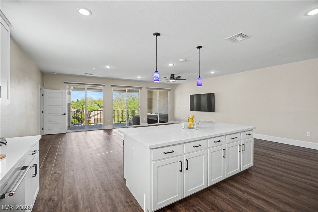 2555 Hampton Road, #11210, Henderson, NV 89052 From the kitchen, the view opens up to the living room, where three sets of sliding glass doors lead out to the balcony with treetop views.