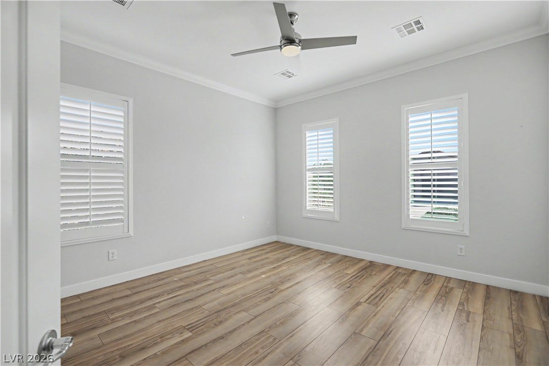 2073 Fountain City Street, Henderson, NV 89052 Three plantation-shuttered windows fill this bedroom with natural light, complemented by crown molding, a modern ceiling fan, and wood-look laminate flooring.