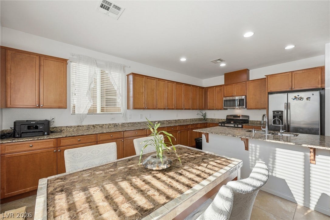 7057 Millers Run Street, North Las Vegas, NV 89084 Ample cabinetry and stone countertops define this kitchen, offering seamless transition to the dining area.