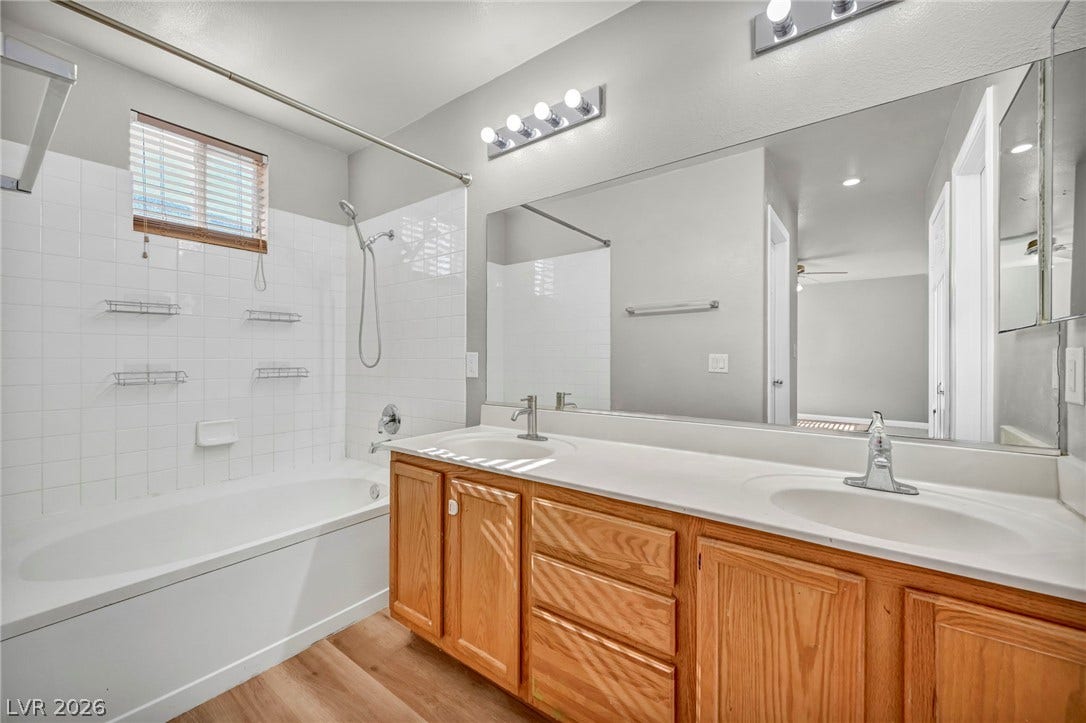 Ample natural light illuminates a wood vanity featuring double sinks alongside a tiled tub shower.