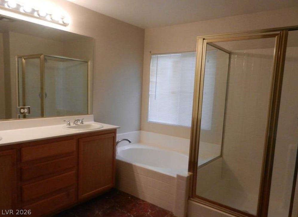 4421 Oberlander Avenue, North Las Vegas, NV 89031 A spacious bathroom features a separate soaking tub and glass-enclosed shower alongside wood cabinetry.