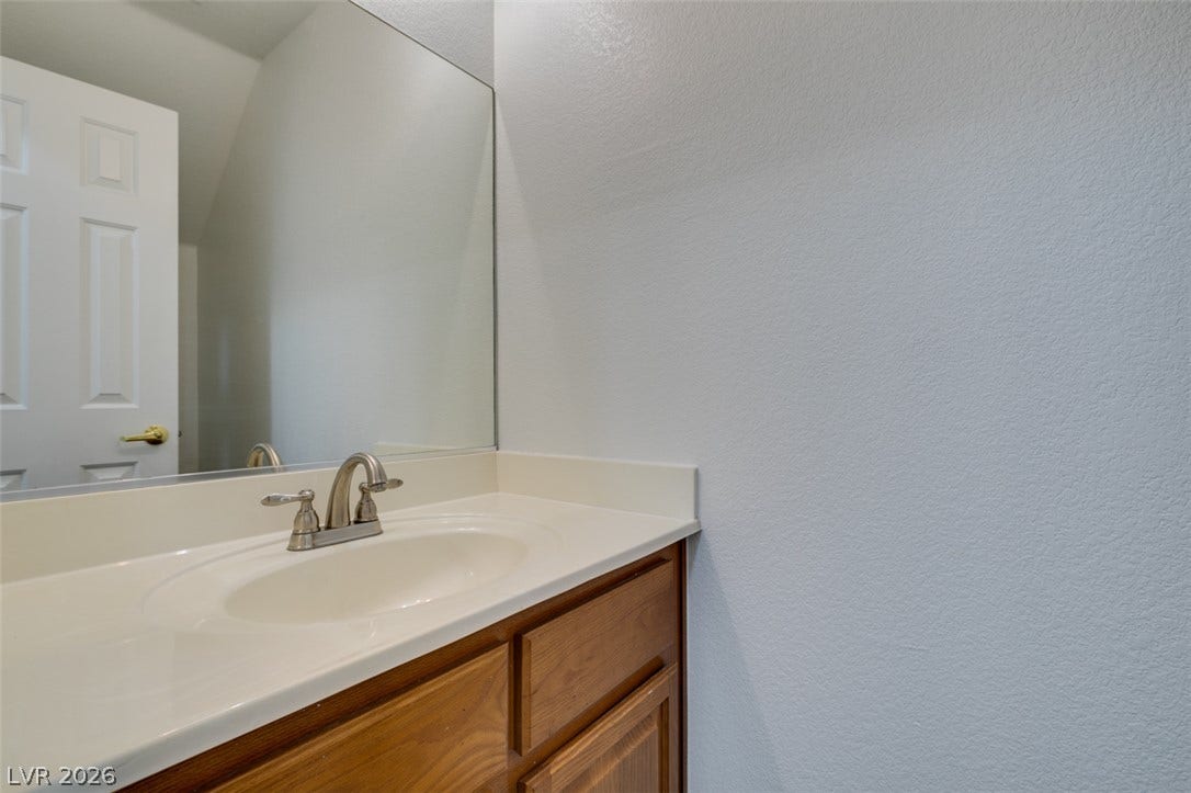 3612 Indigo Flower Street, #2, North Las Vegas, NV 89084 A single vanity with wood cabinetry sits below a large wall mirror.