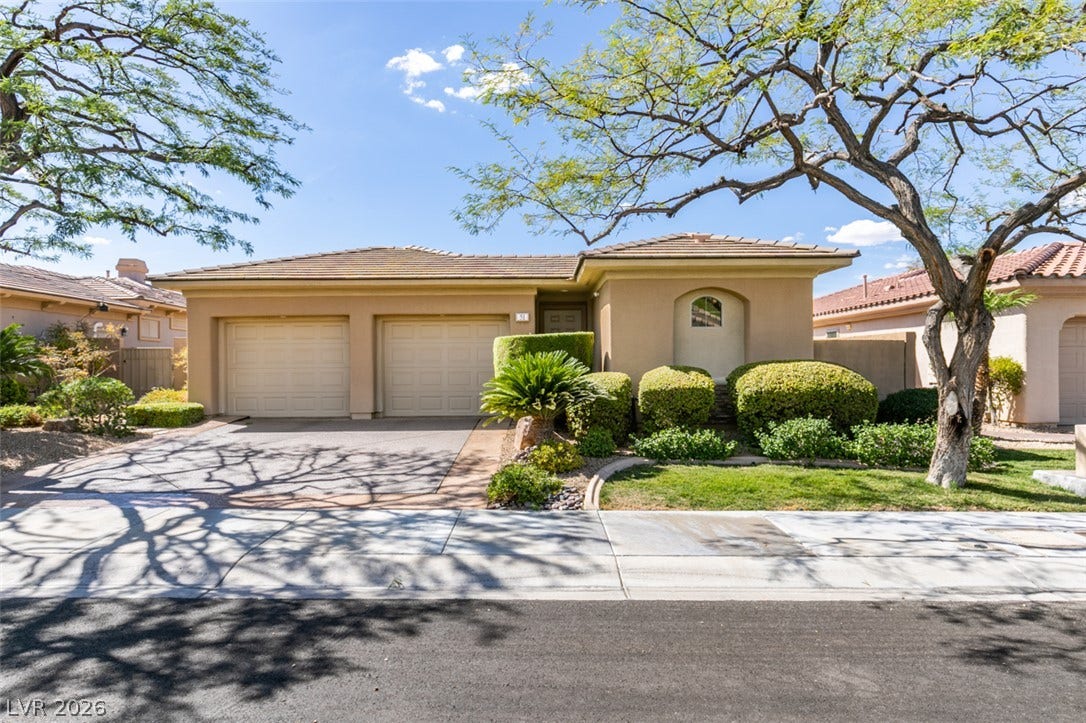 51 E Braelinn Drive, Henderson, NV 89052 Mature trees shade the driveway and front walkway of this stucco home with tile roof.