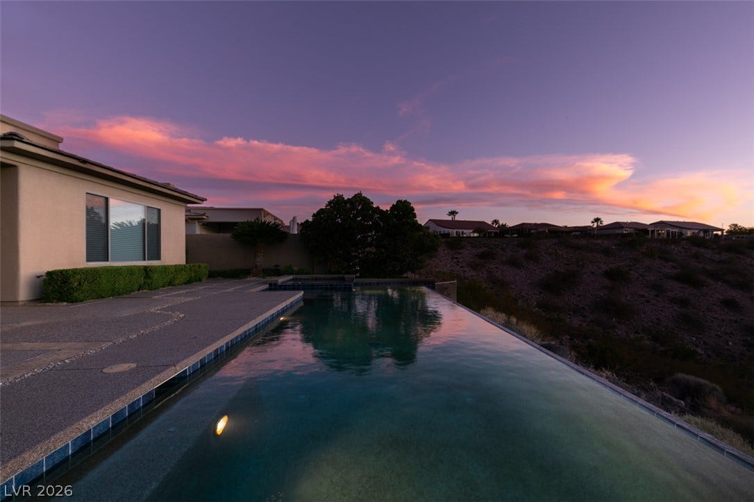 51 E Braelinn Drive, Henderson, NV 89052 An inviting infinity pool overlooks rolling desert hills beneath a vibrant sunset sky.