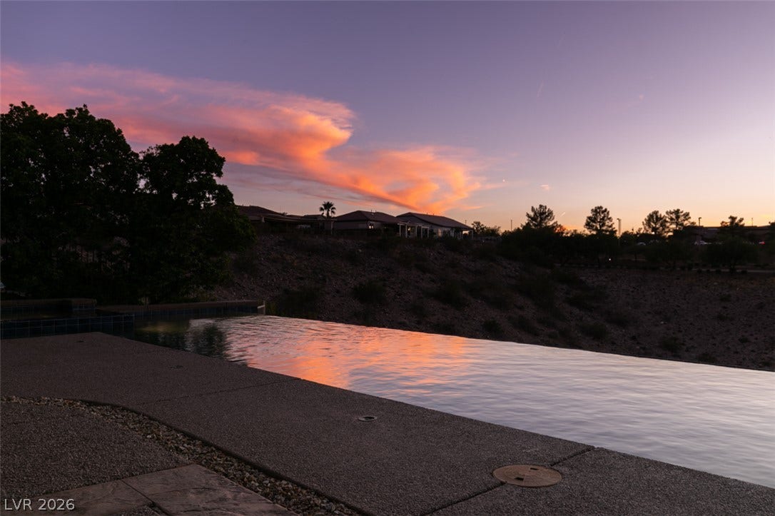 51 E Braelinn Drive, Henderson, NV 89052 An infinity edge swimming pool overlooks rolling hills under a vibrant sunset sky.