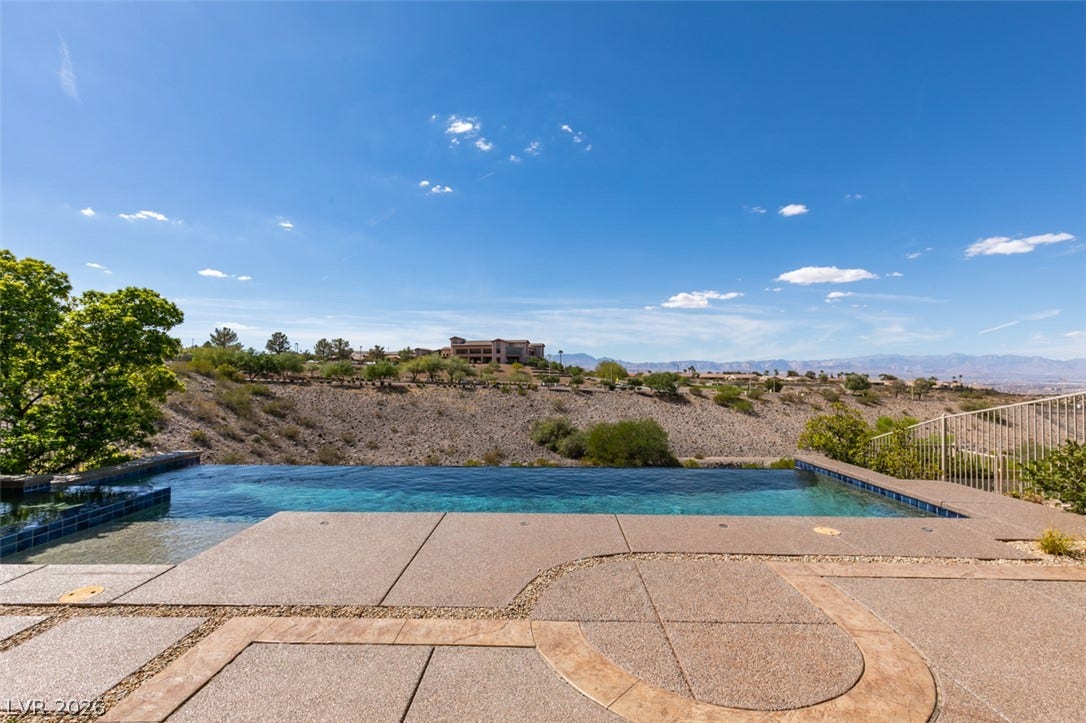 51 E Braelinn Drive, Henderson, NV 89052 An inviting infinity pool overlooks panoramic desert hills and distant mountain peaks under clear blue skies.