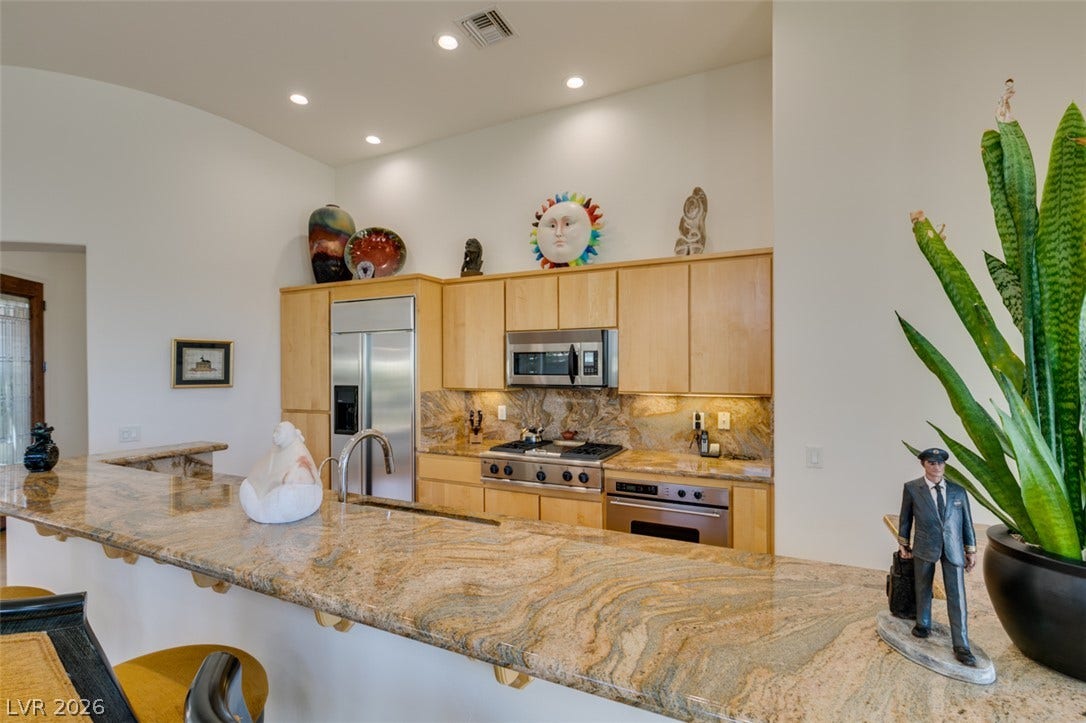 51 E Braelinn Drive, Henderson, NV 89052 Gleaming stone countertops and wood cabinetry define this modern open kitchen space.