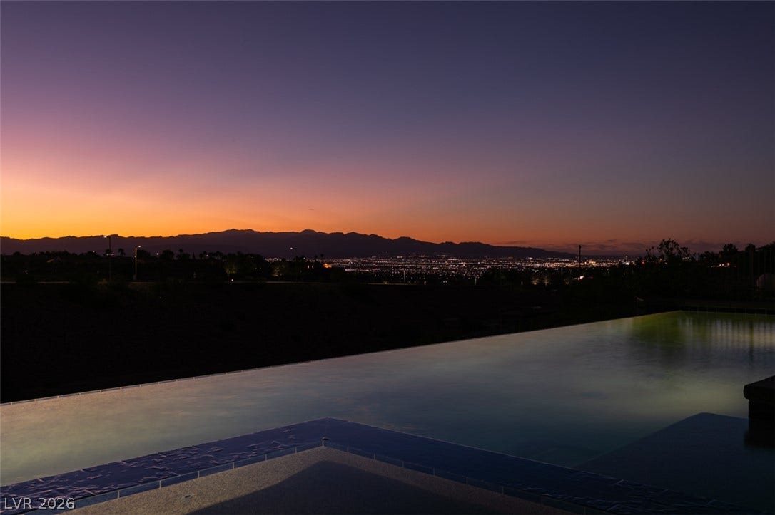 51 E Braelinn Drive, Henderson, NV 89052 Distant city lights and mountain silhouettes frame the peaceful infinity pool during twilight.