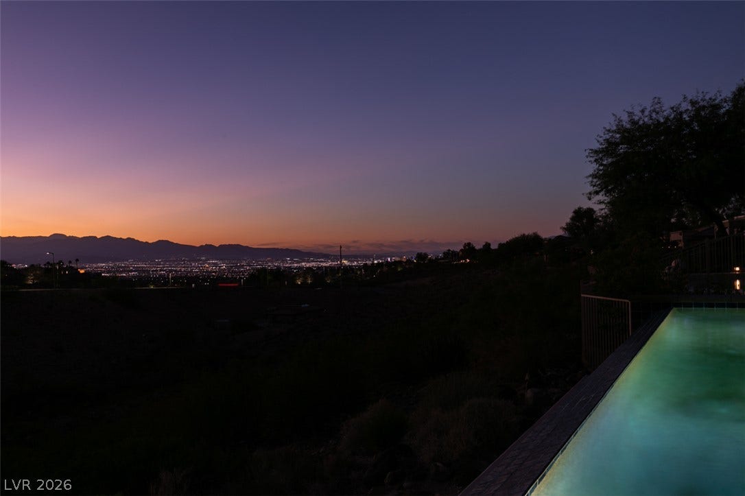51 E Braelinn Drive, Henderson, NV 89052 Glimmering city lights and distant mountain silhouettes frame the illuminated swimming pool at twilight.