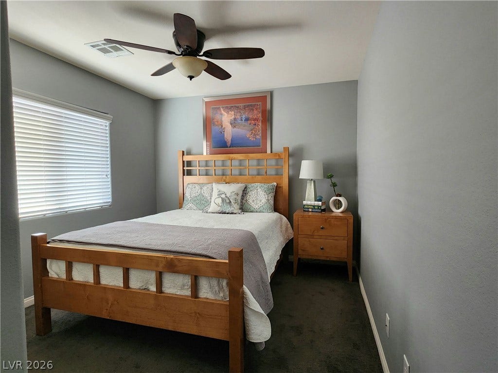10549 Gibbous Moon Drive, Las Vegas, NV 89129 A window with classic blinds illuminates this comfortable bedroom featuring soft carpeted flooring.