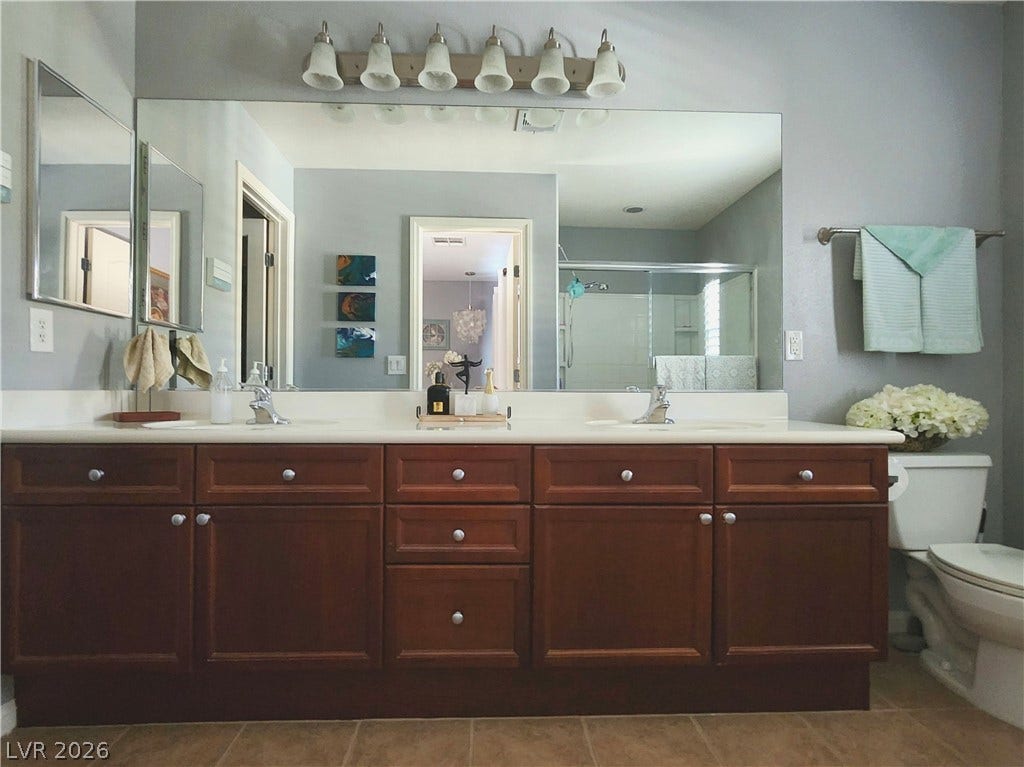 10549 Gibbous Moon Drive, Las Vegas, NV 89129 Warm wood cabinetry and classic tiling define this well-appointed double vanity bathroom.
