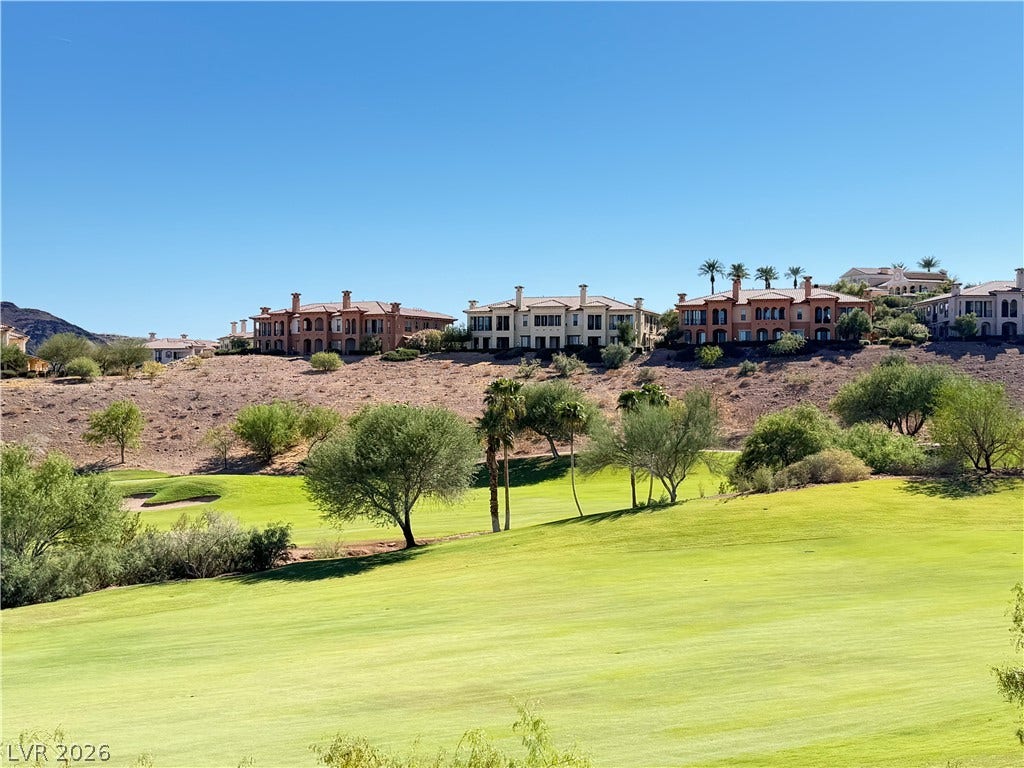 12 Via Visione, #204, Henderson, NV 89011 Expansive green fairways stretch below elevated multi-level residences under a clear blue sky.
