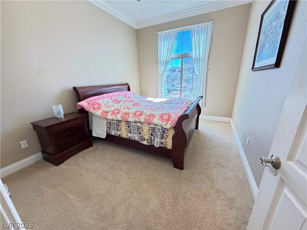 12 Via Visione, #204, Henderson, NV 89011 Plush carpeting and crown molding frame a sunlit bedroom overlooking scenic distant hills.