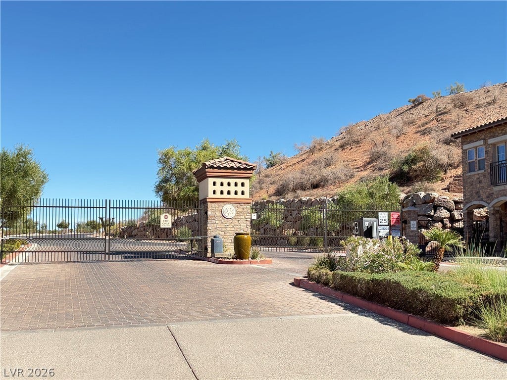 12 Via Visione, #204, Henderson, NV 89011 A secure gated entrance features stone pillars and wrought iron gates set against a hillside backdrop.