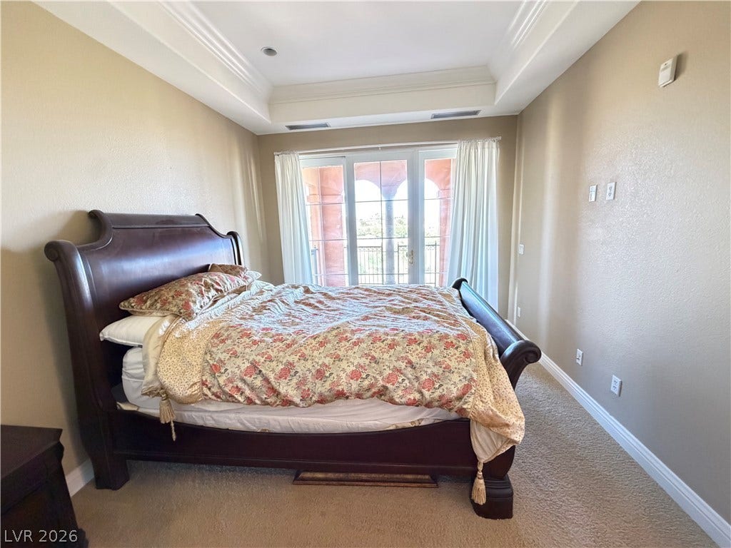12 Via Visione, #204, Henderson, NV 89011 Crown molding and a tray ceiling elevate this carpeted bedroom featuring private balcony access.