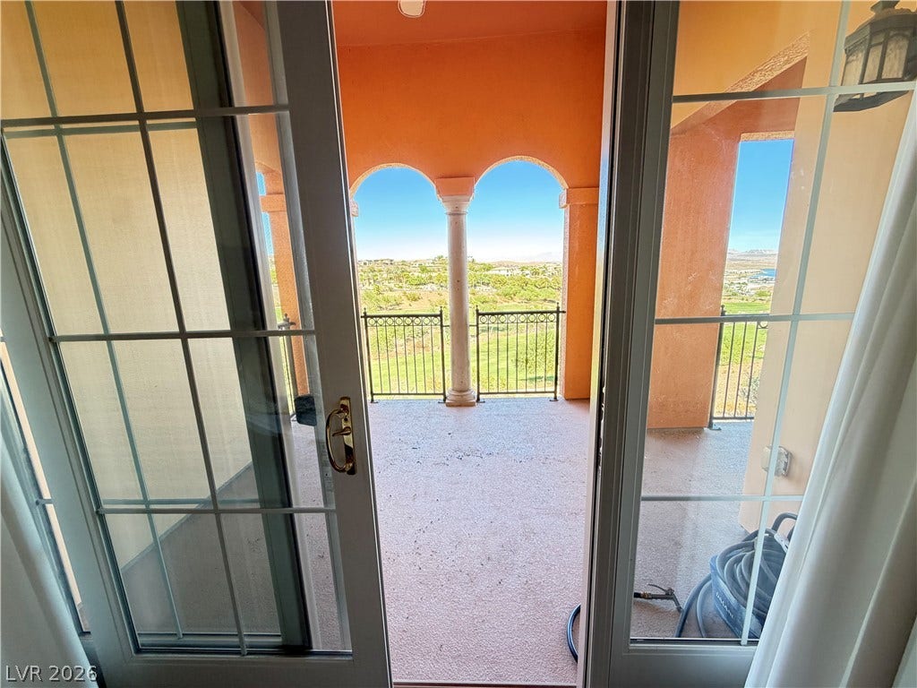 12 Via Visione, #204, Henderson, NV 89011 Double glass doors open to a covered balcony showcasing scenic valley views framed by arches.