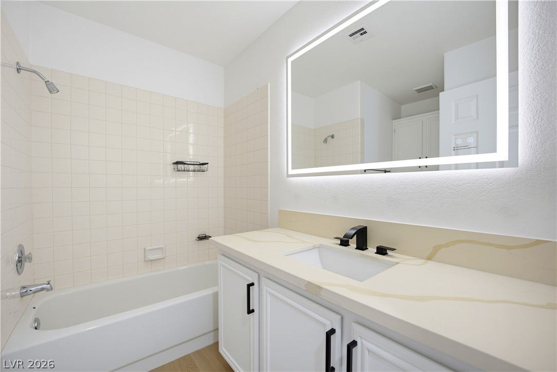 4722 Casa Bonita Drive, North Las Vegas, NV 89032 An integrated LED mirror illuminates the stone-topped vanity adjacent to a tiled tub shower.