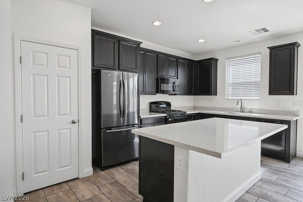 A spacious central island anchors this modern kitchen with dark cabinetry and tile floors.