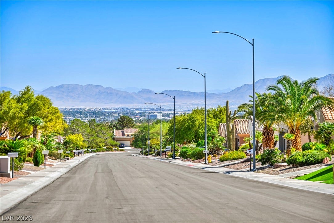 10020 Villa Ridge Drive, Las Vegas, NV 89134 Majestic mountain ridges frame the distant horizon beyond a quiet, palm-lined suburban streetscape.
