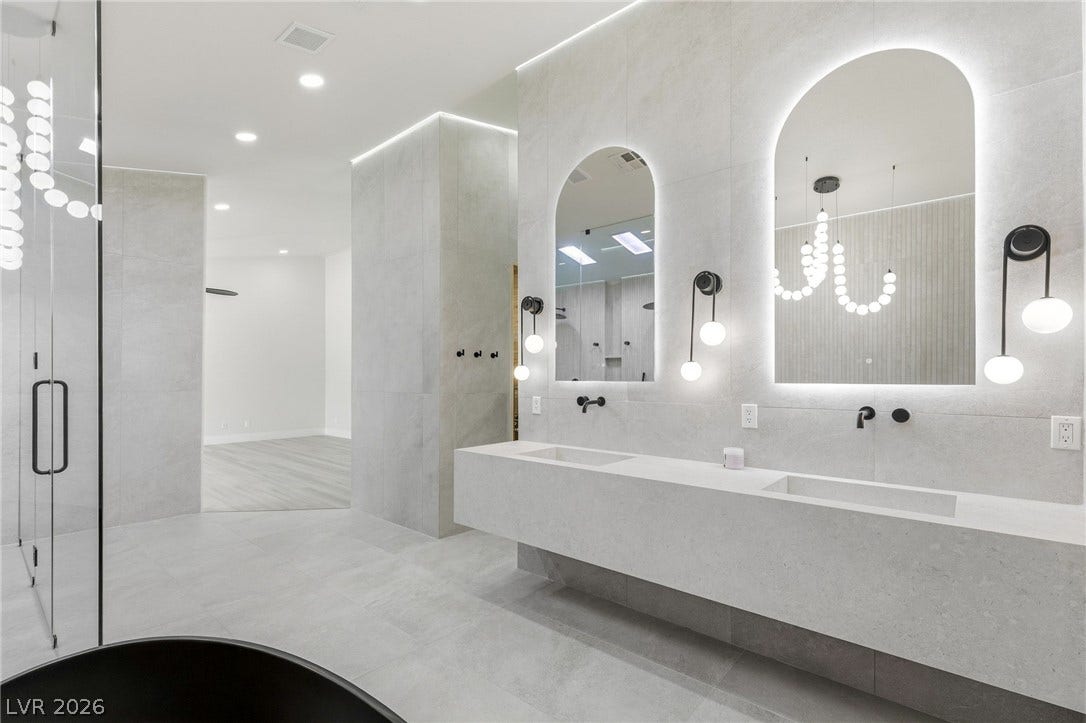10626 San Vercelli Court, Las Vegas, NV 89141 A floating dual vanity and arched backlit mirrors highlight this modern primary bathroom.