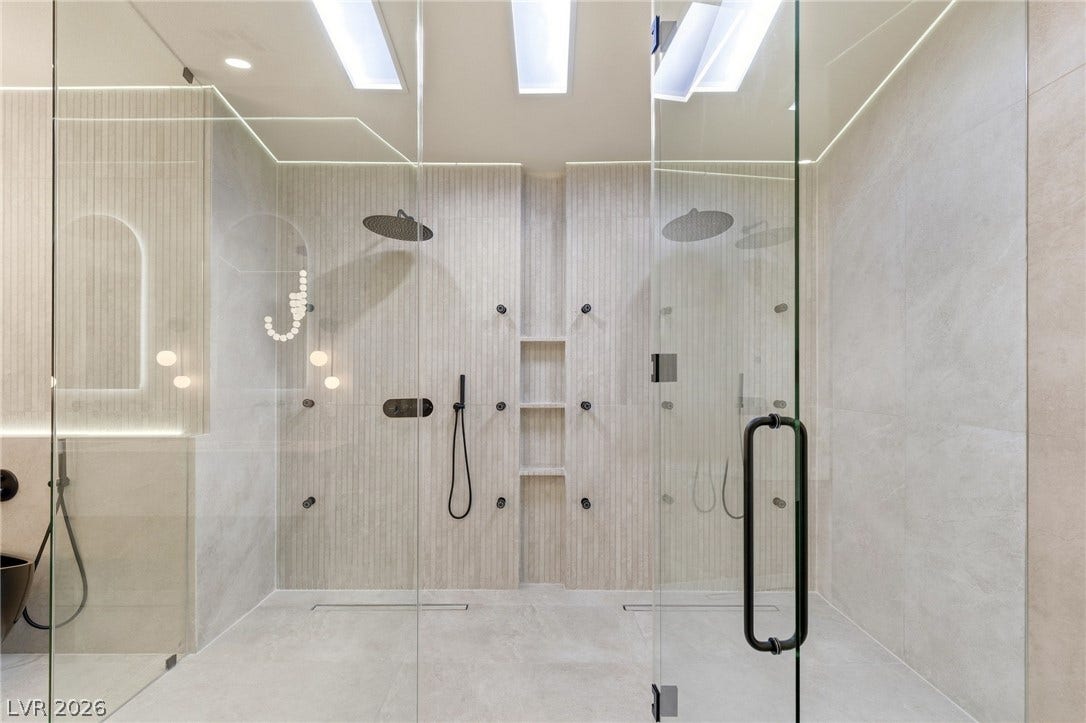 10626 San Vercelli Court, Las Vegas, NV 89141 A glass-enclosed shower showcases dual rainfall heads, body jets, and built-in shelving.