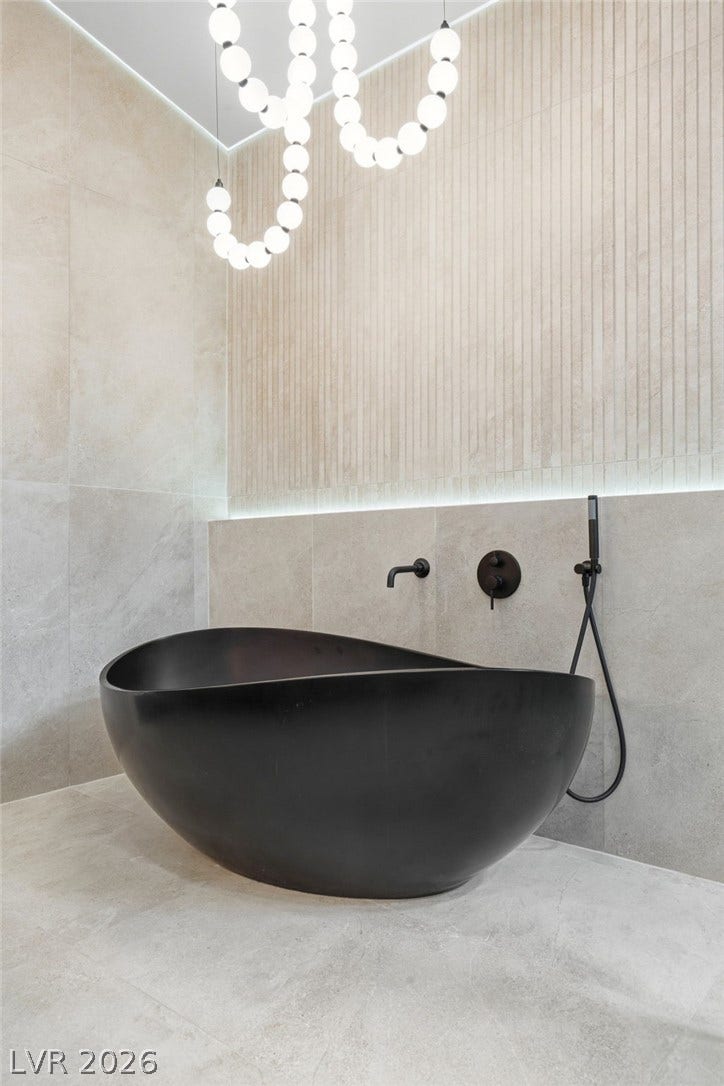 10626 San Vercelli Court, Las Vegas, NV 89141 Smooth tiled surfaces surround a deep freestanding soaking tub, illuminated by custom ceiling fixtures.
