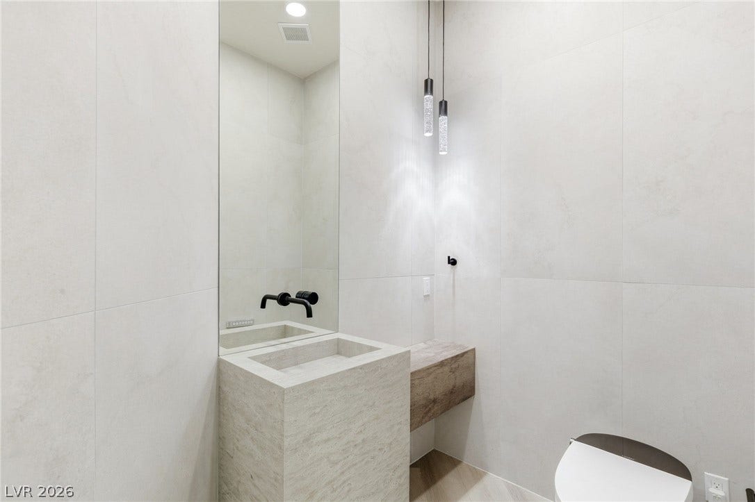 10626 San Vercelli Court, Las Vegas, NV 89141 Floor-to-ceiling tiles and a custom stone pedestal sink define this minimalist powder room.
