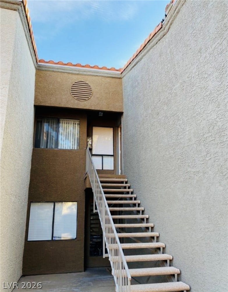 An outdoor staircase leads to the upper level entry of this stucco exterior.