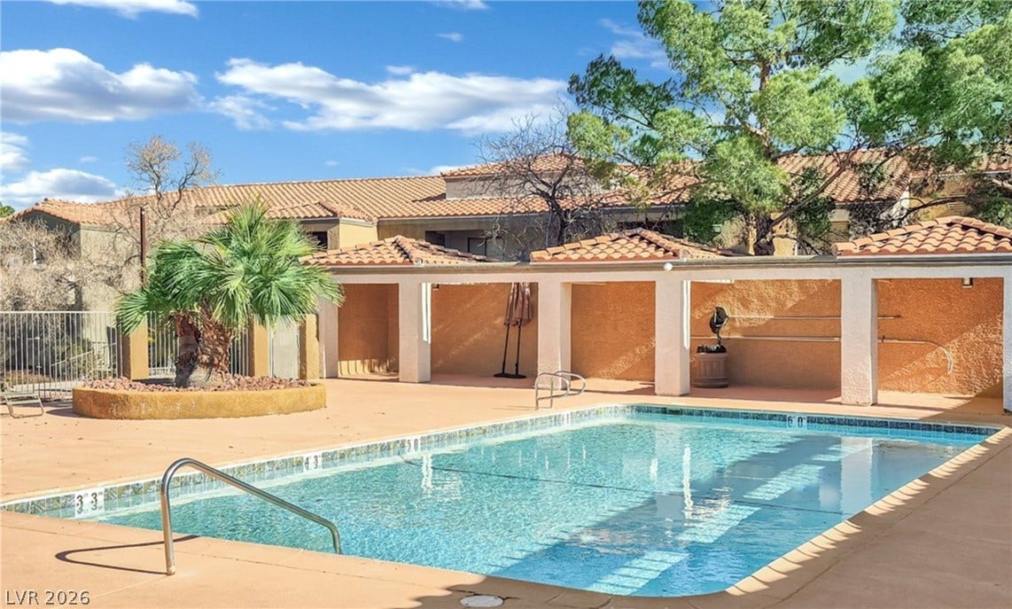 A sparkling outdoor pool sits framed by classic tiled roofs and mature desert trees.