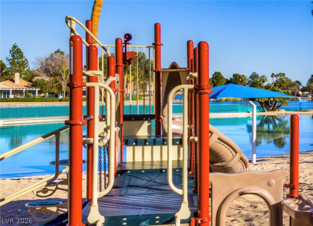 A vibrant lakeside recreational area features a sandy playground bordering calm blue waters.