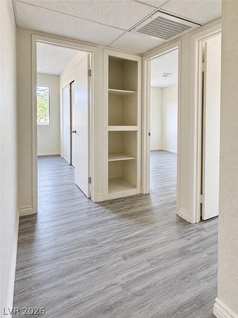 Modern wood-look flooring and built-in shelving anchor this bright hallway connecting several rooms.