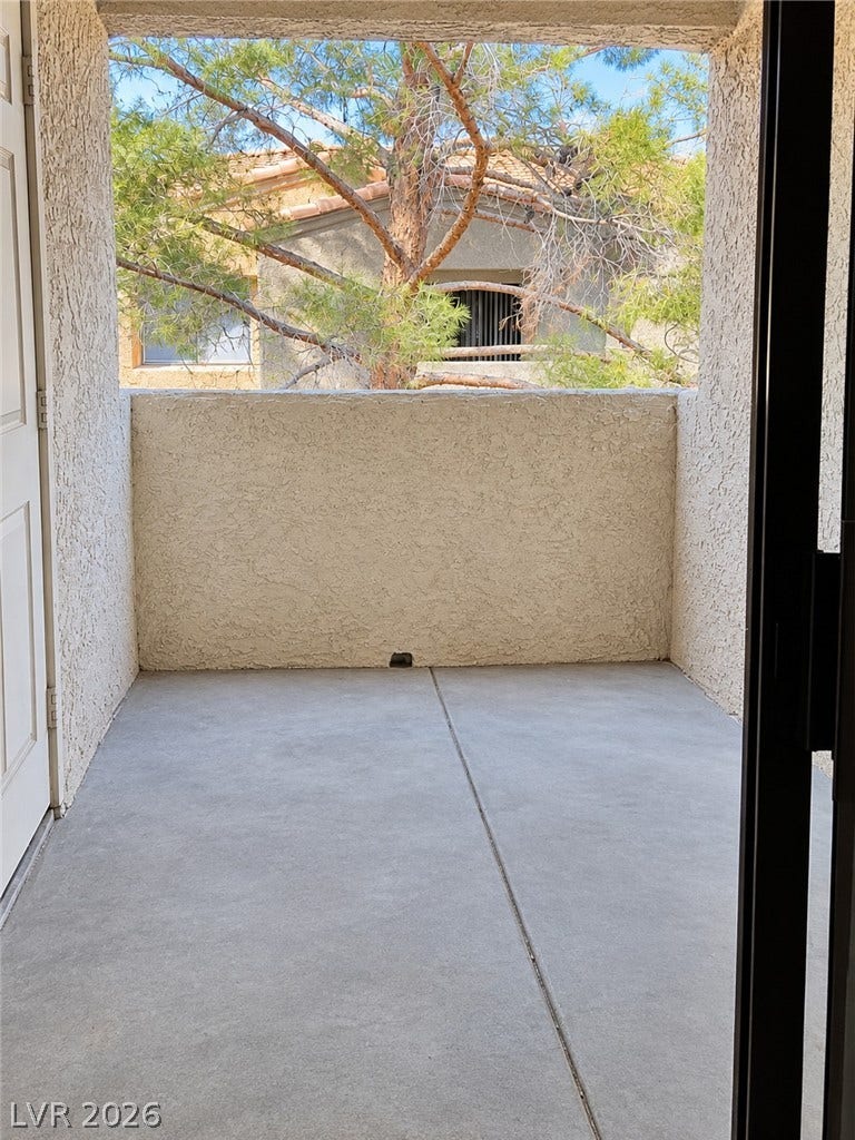 An inviting covered balcony features durable concrete flooring and textured walls overlooking mature green trees.