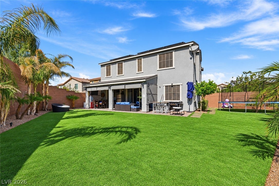 31 Cresta Villa Court, Henderson, NV 89011 A spacious backyard features manicured synthetic turf alongside a covered patio and modern exterior stucco.